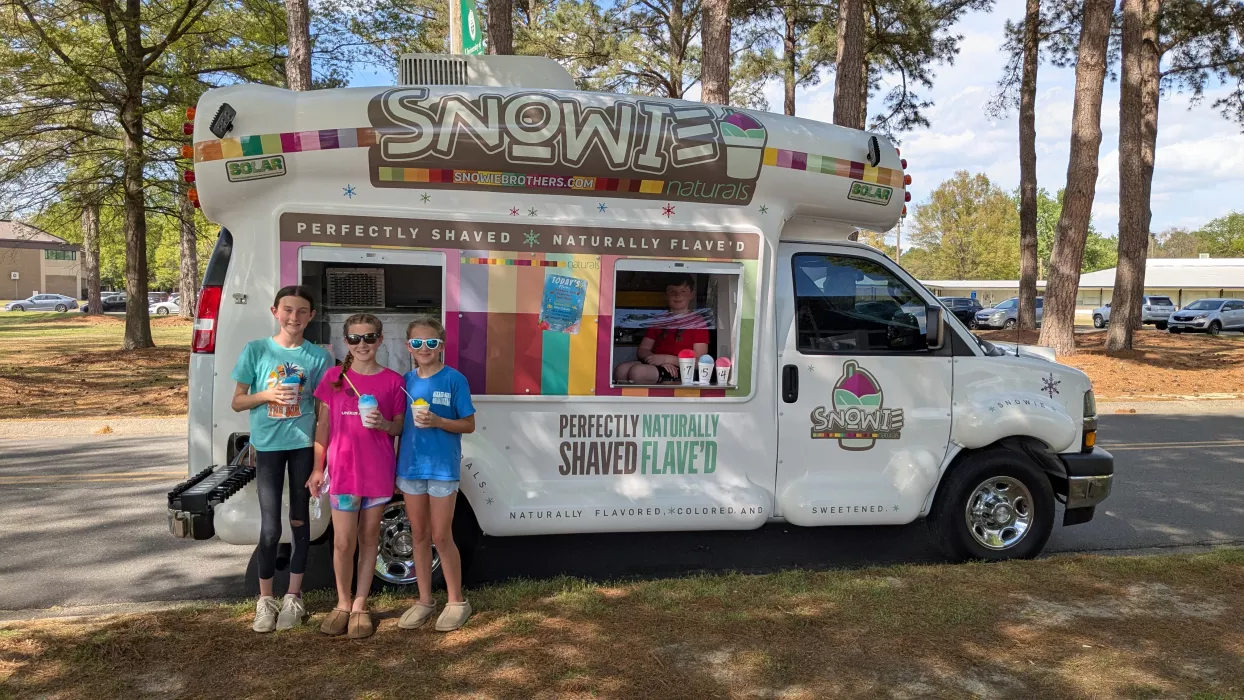 Three smiling girls wearing sunglasses, enjoying colorful shaved ice in front of the Snowie Brothers Shaved Ice Truck. Perfect for summer events, the truck serves refreshing, fun, and tasty shaved ice treats for all ages!