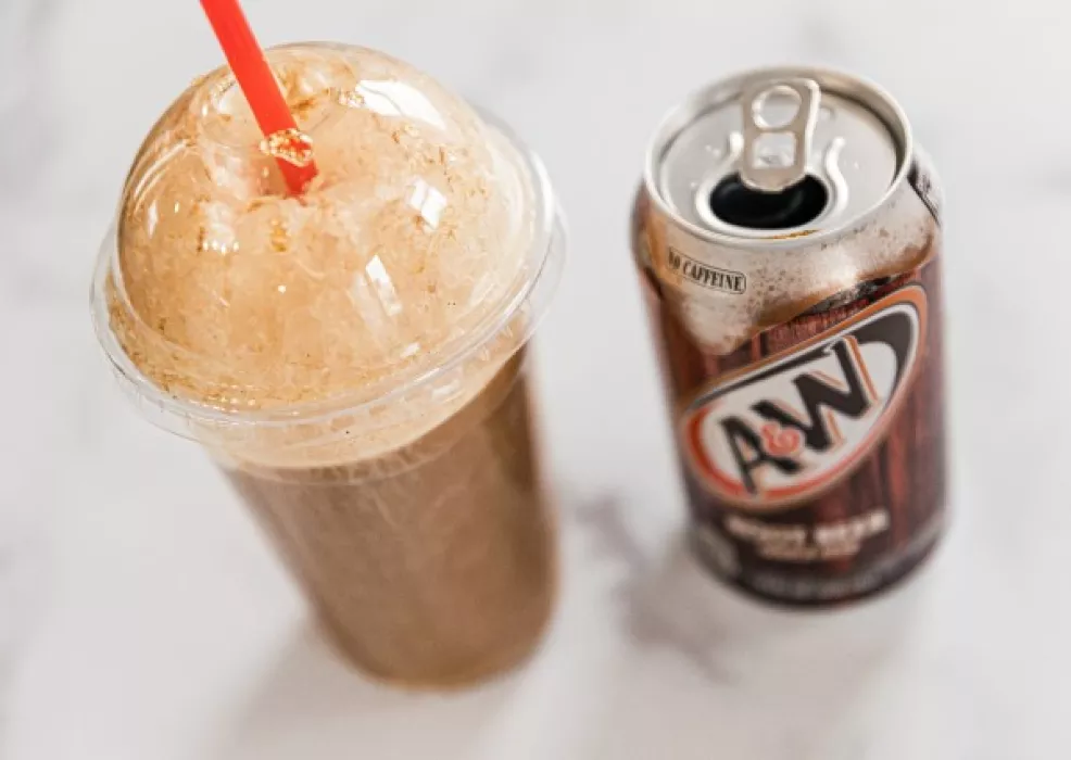 Root beer float with vanilla ice cream in a cup with lid and straw next to a can of A&amp;W root beer